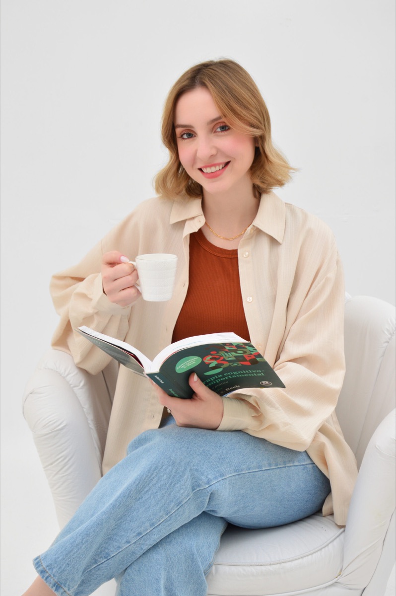 Gabriela Bobsin Cerentini, psicóloga CRP 07/45222, sorrindo com um livro de Terapia Cognitivo-Comportamental